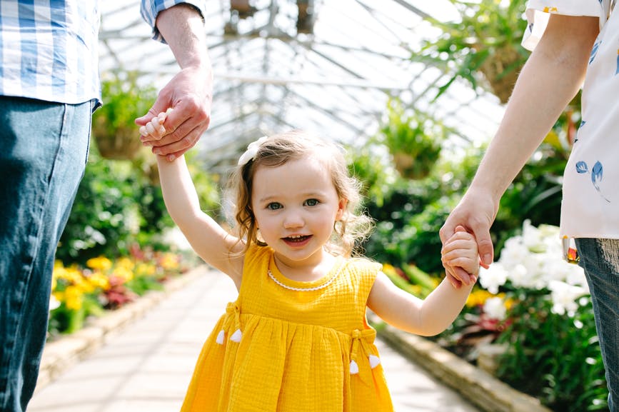 toddler girl yellow dress holding hands parents mom dad mother father flowers greenhouse walking summer